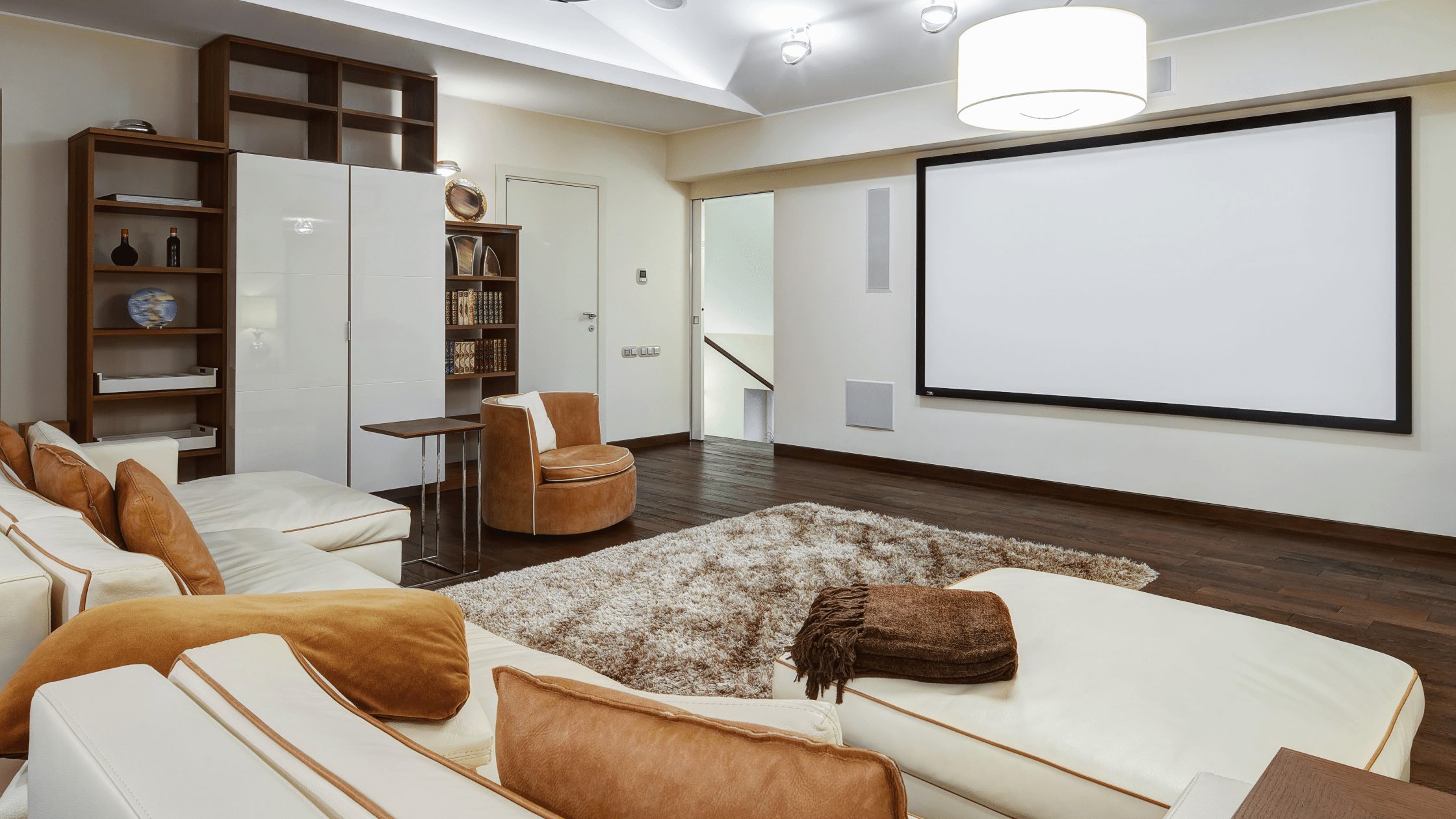 Home theater with a large projection screen, cream sectional seating, brown cushions and built-in shelving.