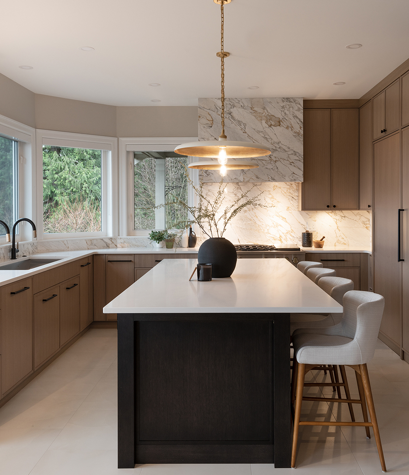 Kitchen with a dark island, upholstered counter stools, wood cabinetry and brass-toned pendant lights