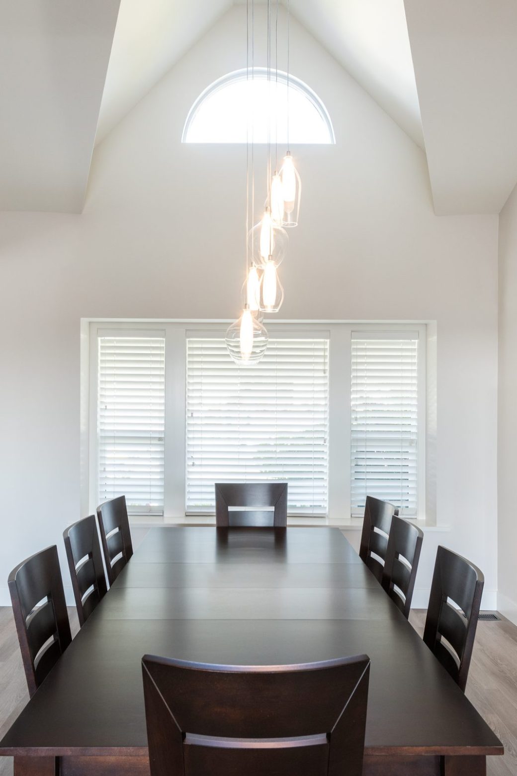 Dining room with a dark table, hanging glass lights, tall vaulted ceiling and a wall-mounted fireplace.
