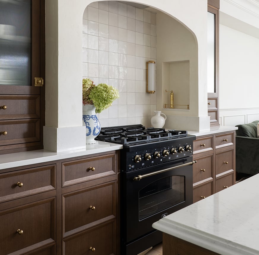 Black range in a white arched alcove with square tile backsplash and wood cabinets.
