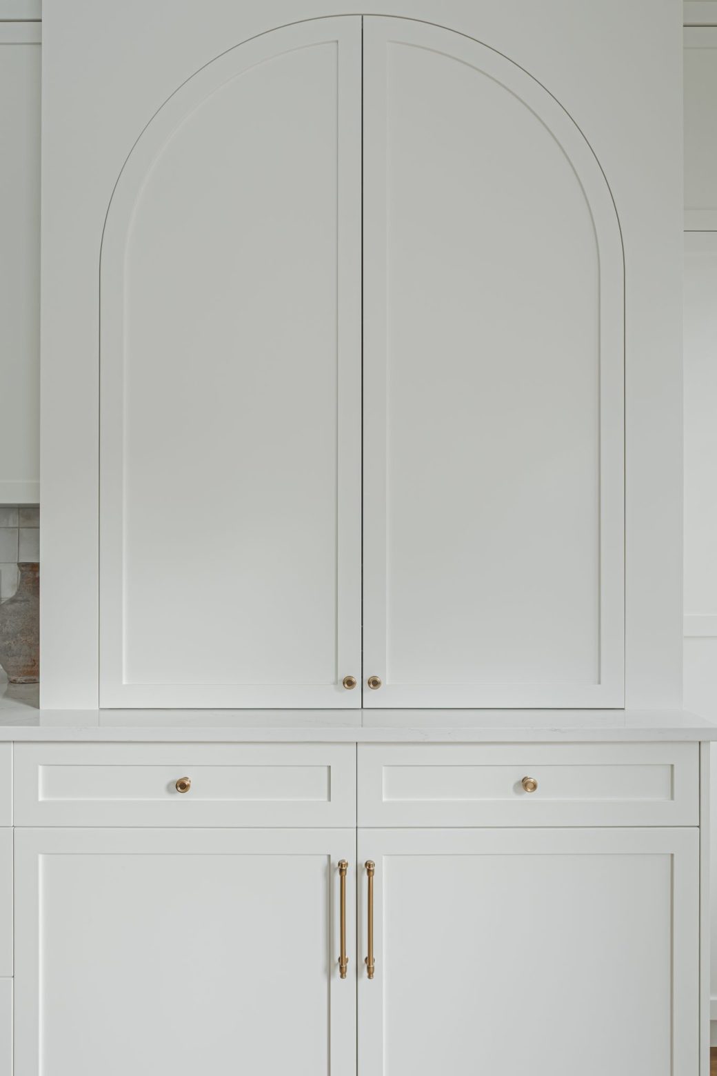 Hidden in Plain Sight white kitchen cabinetry with arched upper doors and brass hardware