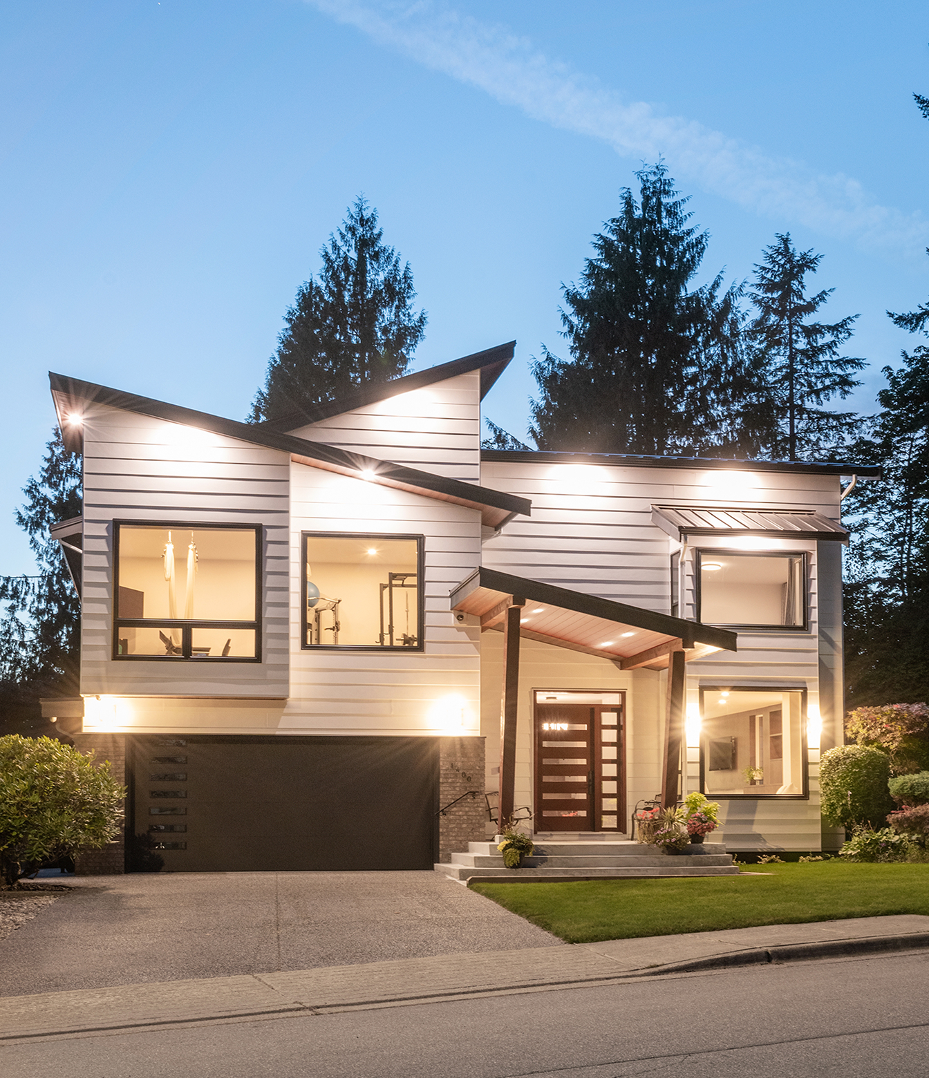 The Rebuild exterior with angular rooflines, illuminated windows and an attached garage at dusk