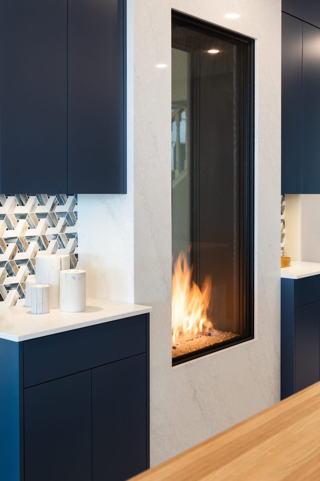 Tall glass-front fireplace framed by a pale surround and blue kitchen cabinets.