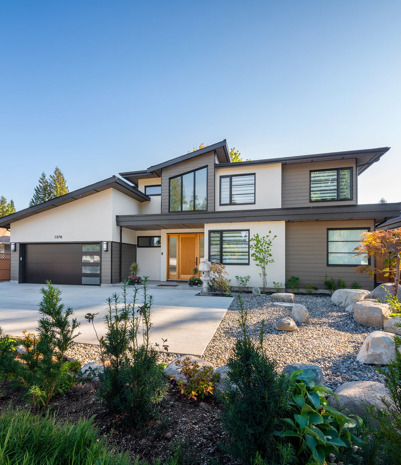 House exterior with angled rooflines, grey siding, a wood entry door, double garage and boulder landscaping.