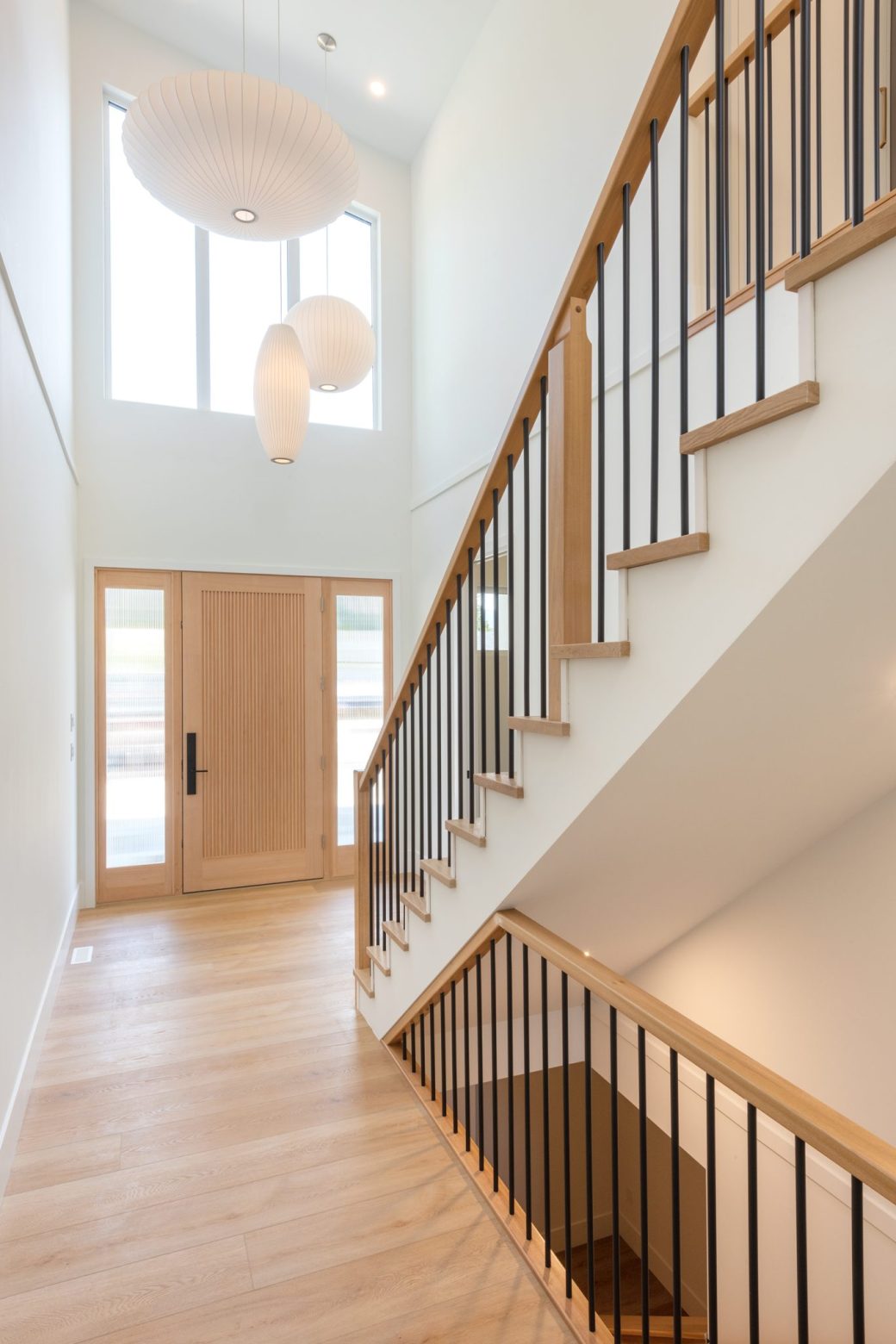 Double-height entry with wood stairs, black balusters and three sculptural pendant lights.