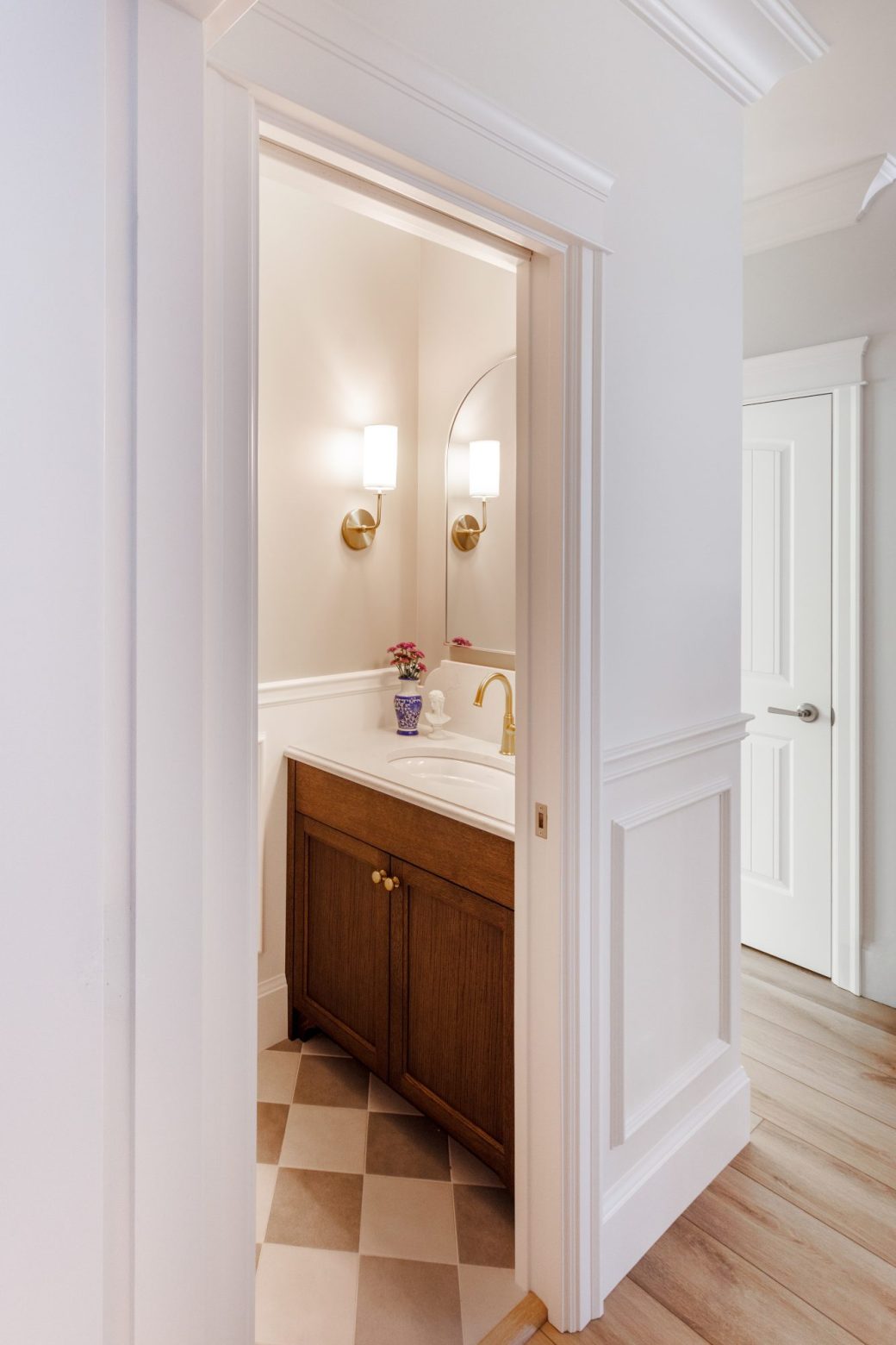 View through a doorway into a powder room with a wood vanity, brass-colored fixtures and checkerboard floor.