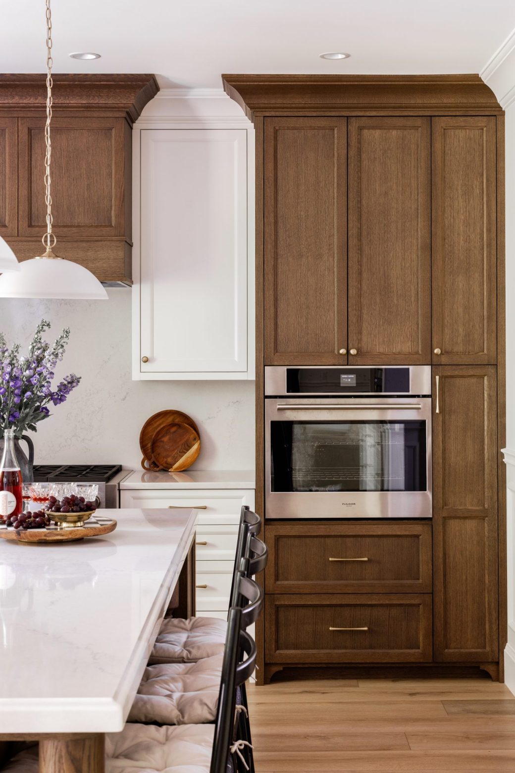Built-in stainless steel oven surrounded by tall wood cabinets beside the kitchen island.
