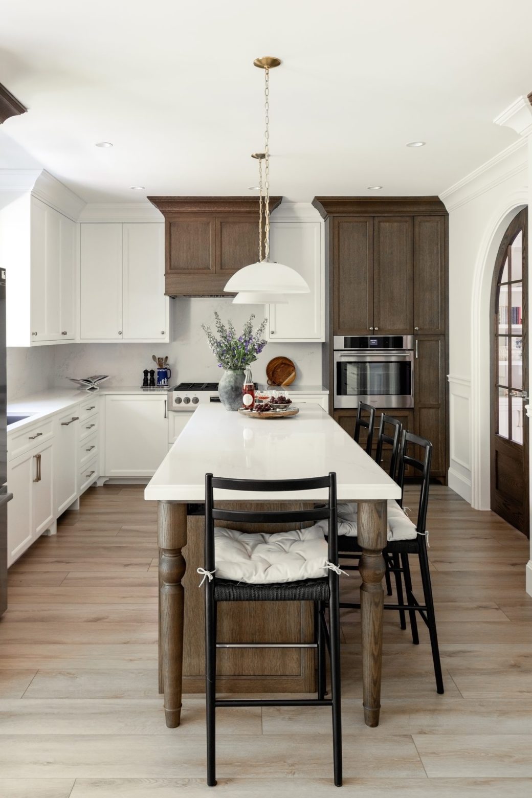 Kitchen with a long white-topped island, black counter stools, white cabinets and wood accents.