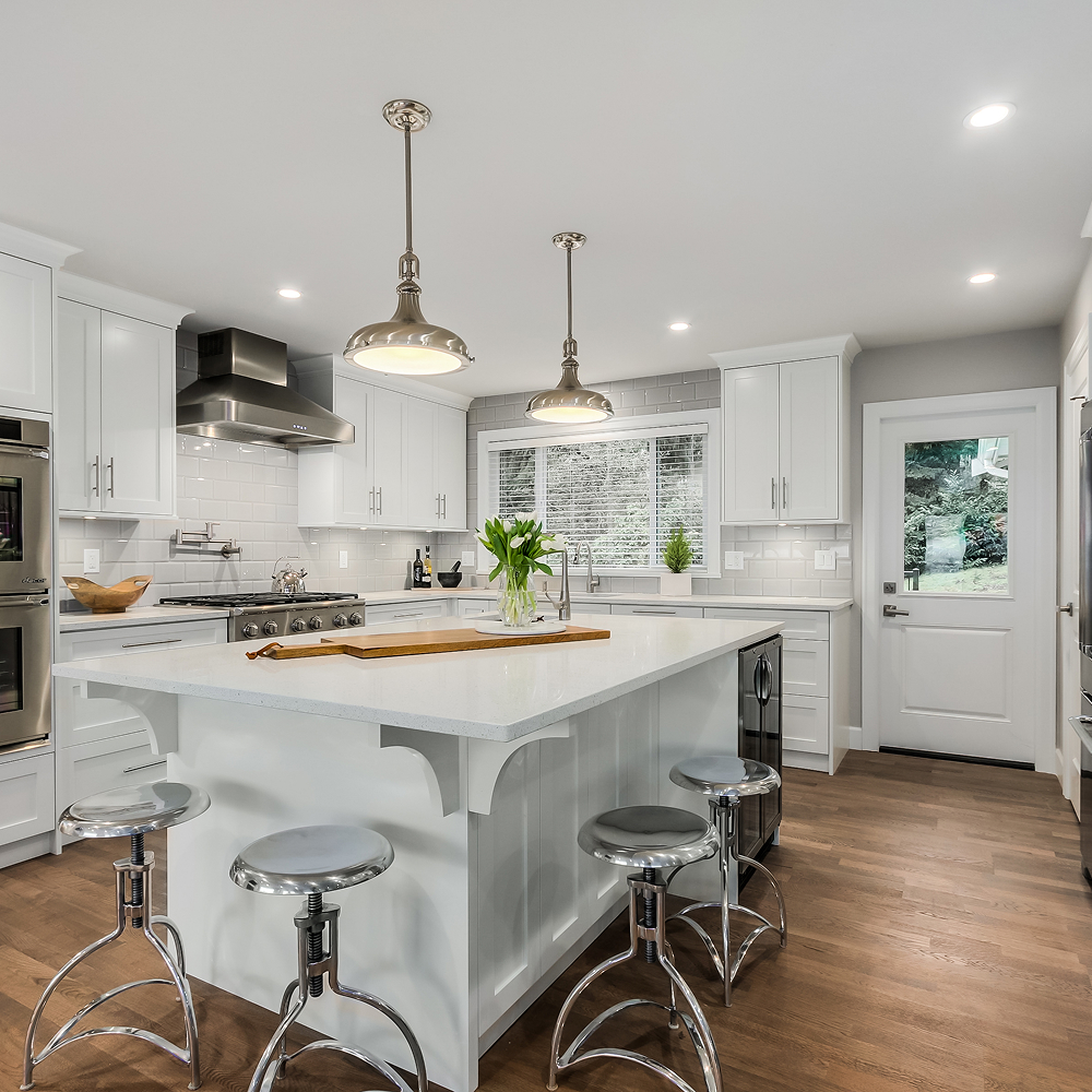 The Canopy View white kitchen with a central island, metal stools and pendant lights