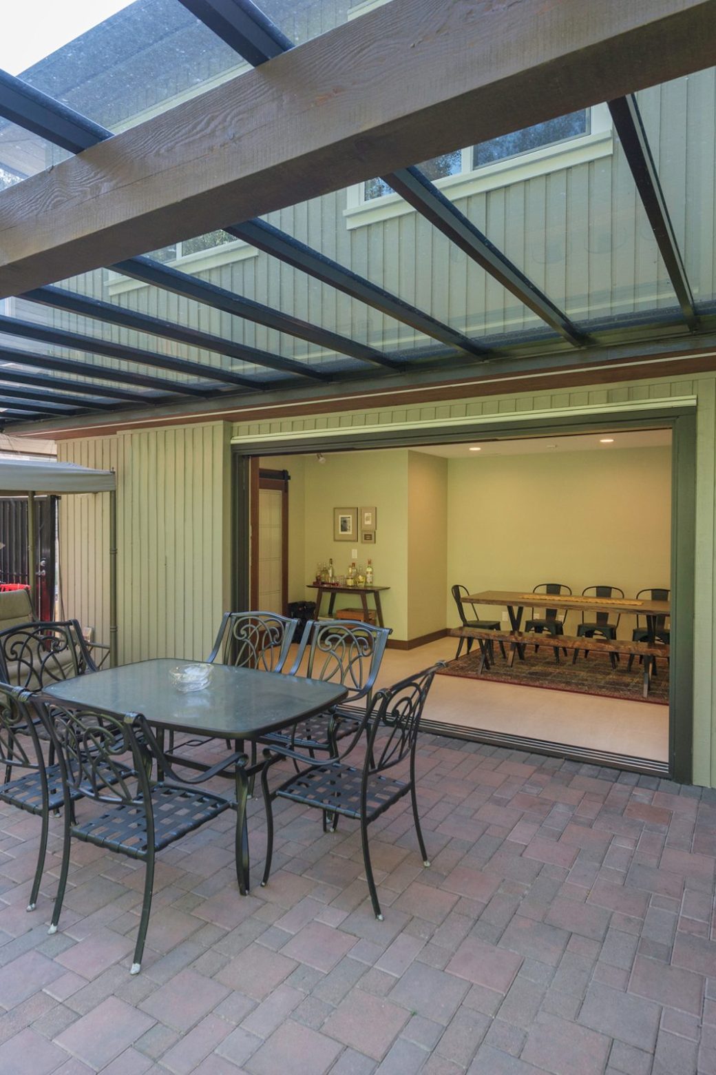 Covered patio with a dining set, garden swing and wide opening to the indoor dining room.