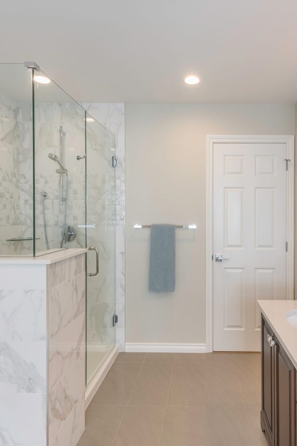 Bathroom with a glass-enclosed shower, pale veined tile, bathtub and dark wood vanity.