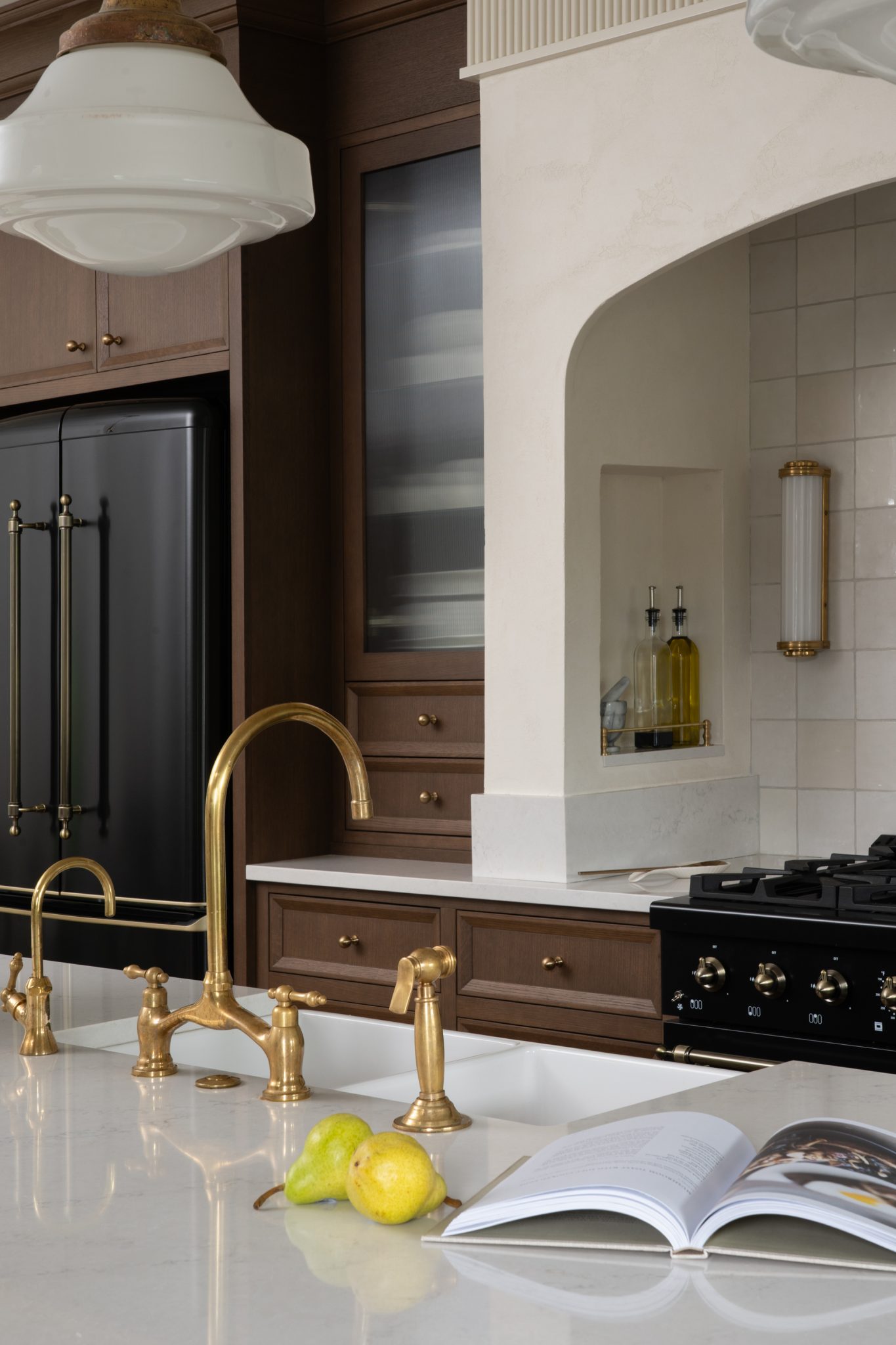 Gold-toned bridge faucet and white countertop in front of wood cabinets and an arched range alcove.