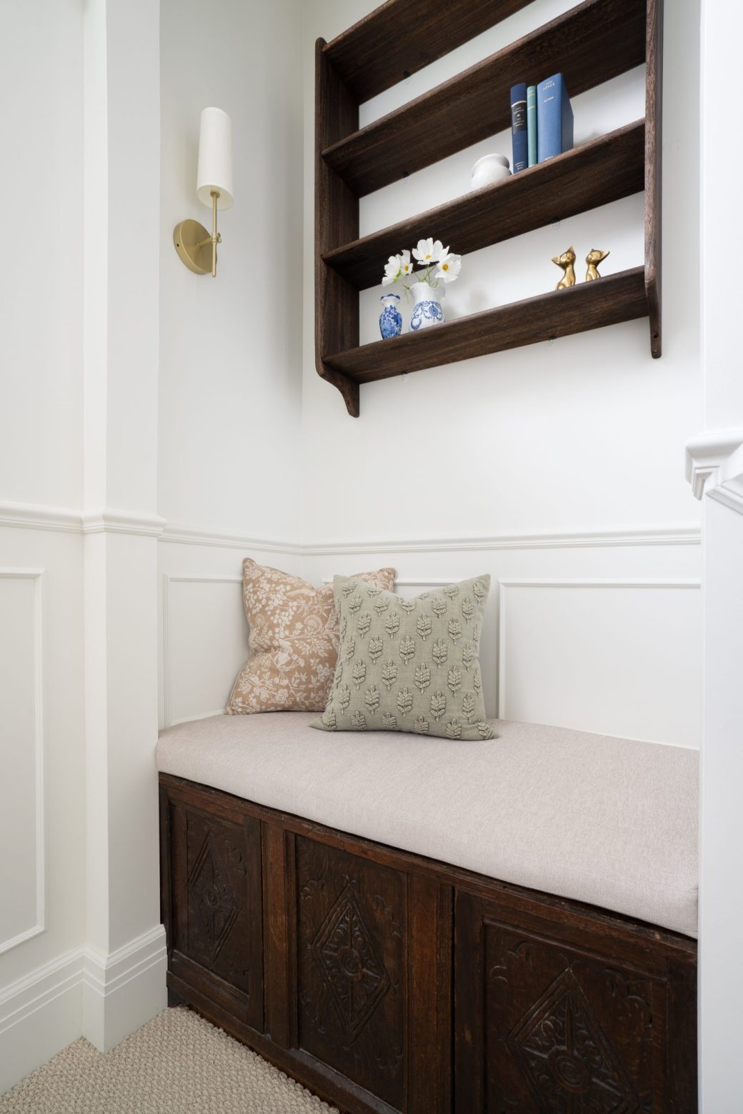 Cushioned bench with carved wood storage panels beneath a wall shelf and sconce.