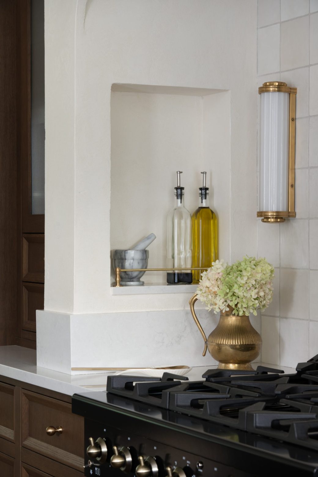 Recessed shelf with oil bottles beside a wall sconce and black kitchen range.