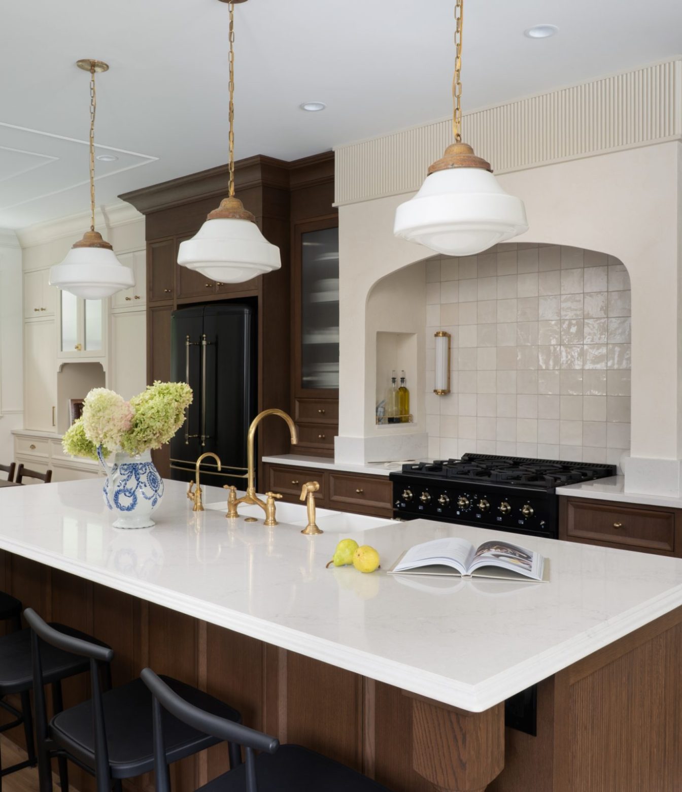 Wood kitchen with a white-topped island, black stools and an arched range alcove beneath three pendant lights.