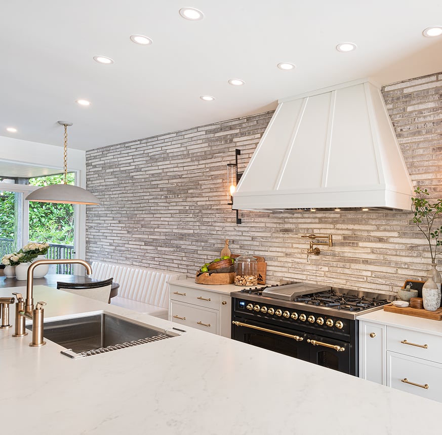 White kitchen sink island facing a black range, pale brick backsplash and breakfast nook.