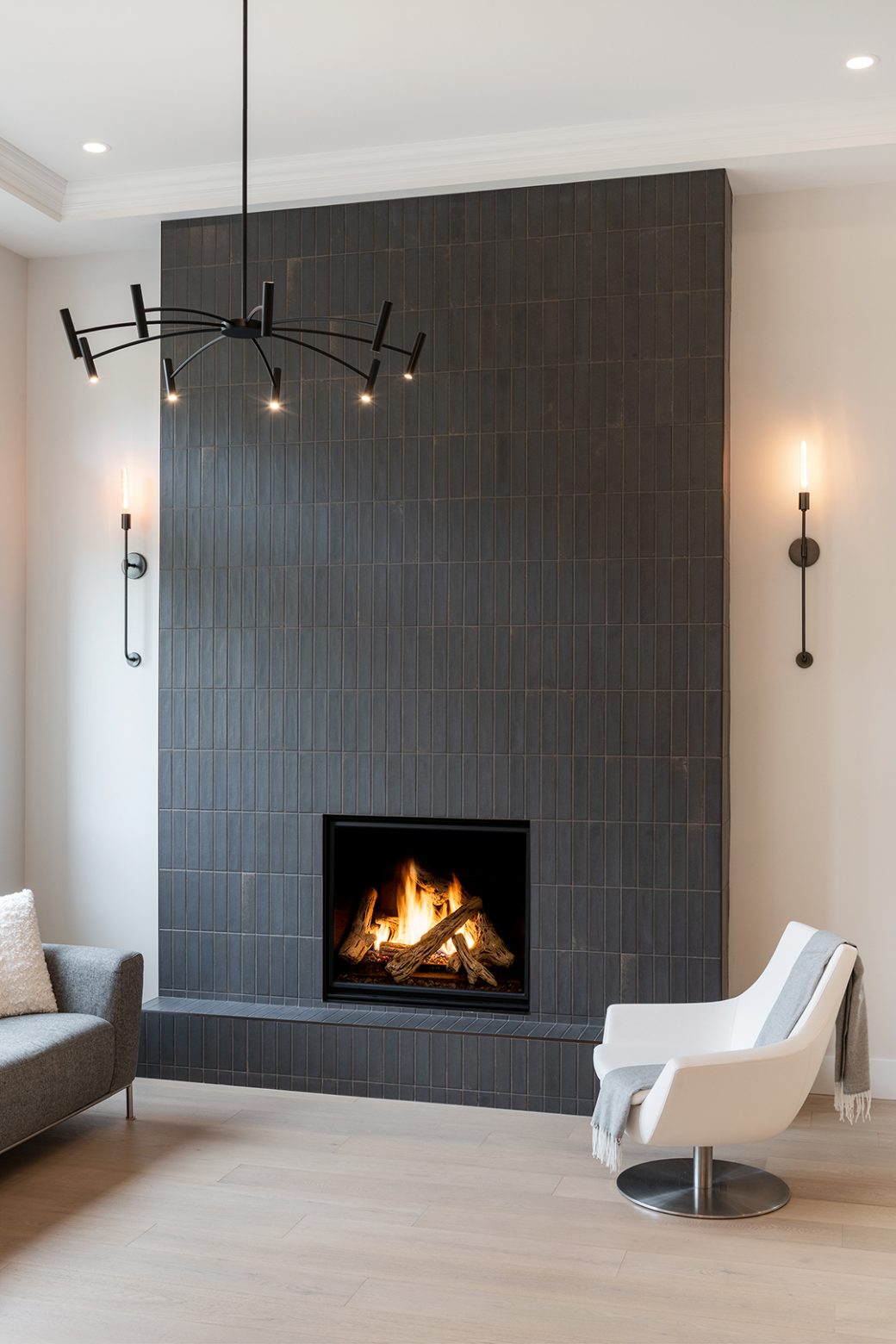 Floor-to-ceiling dark tiled fireplace with wall sconces and a white lounge chair.