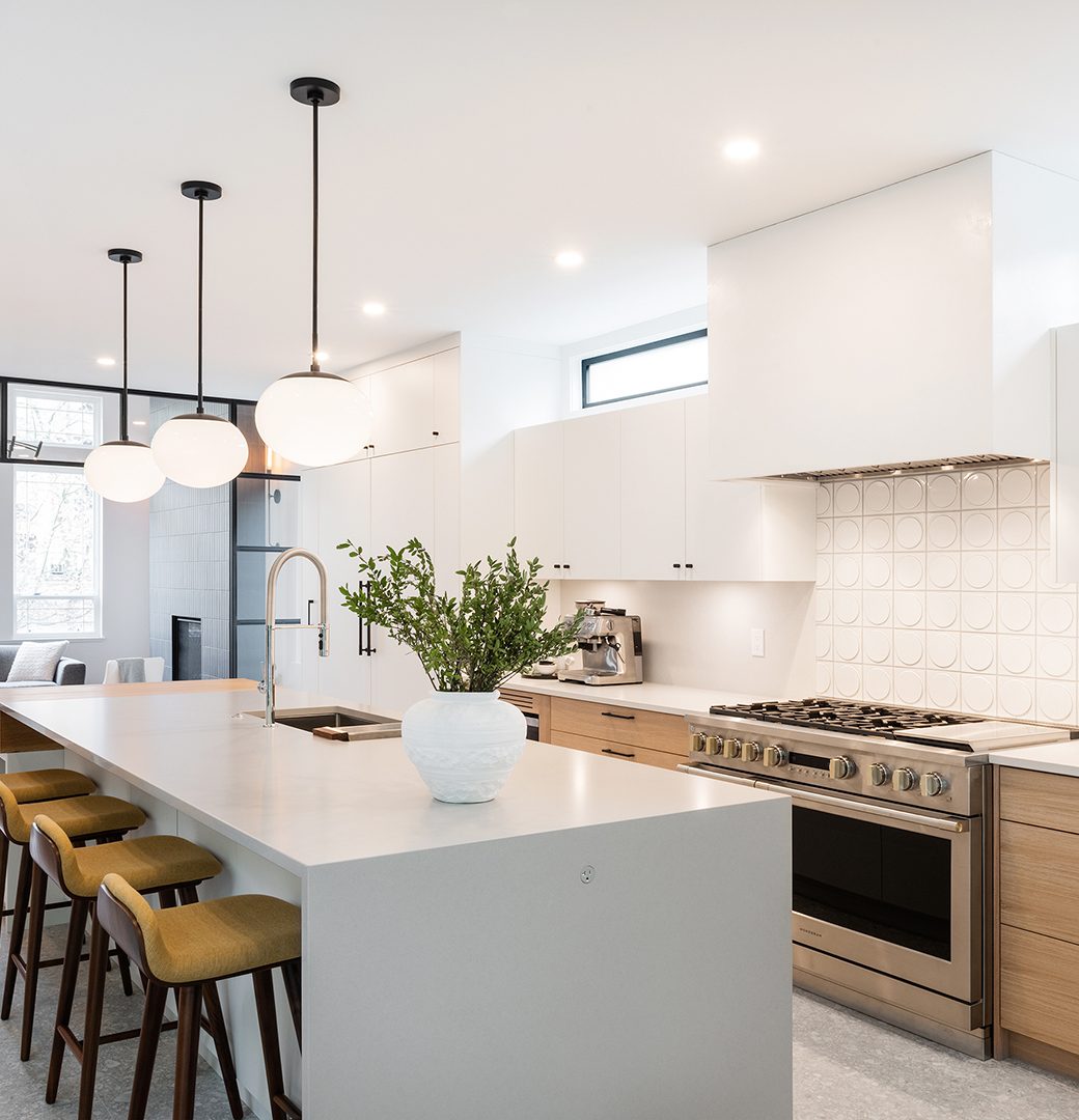 Kitchen with a white waterfall island, three bar stools, wood drawers and globe pendant lights.