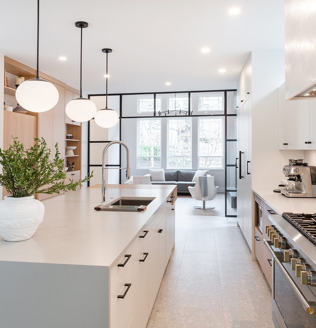 White kitchen island and stainless steel range beneath globe pendant lights, facing a black-framed glass partition.
