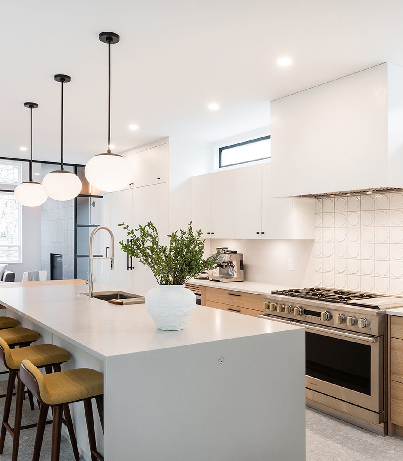 Kitchen with a white waterfall island, wood drawers, mustard stools and three globe pendant lights.